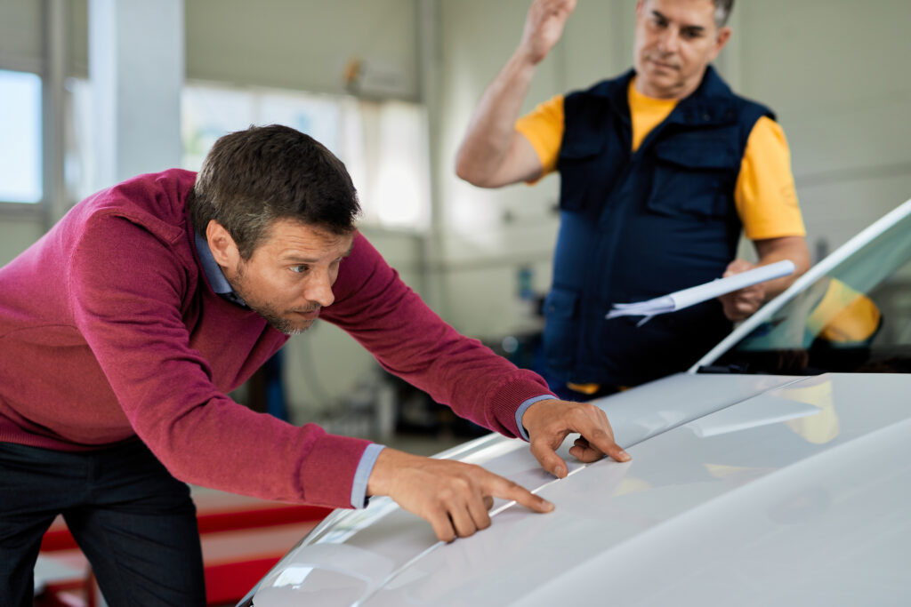 Male customer examining car hood while being in auto repair shop.